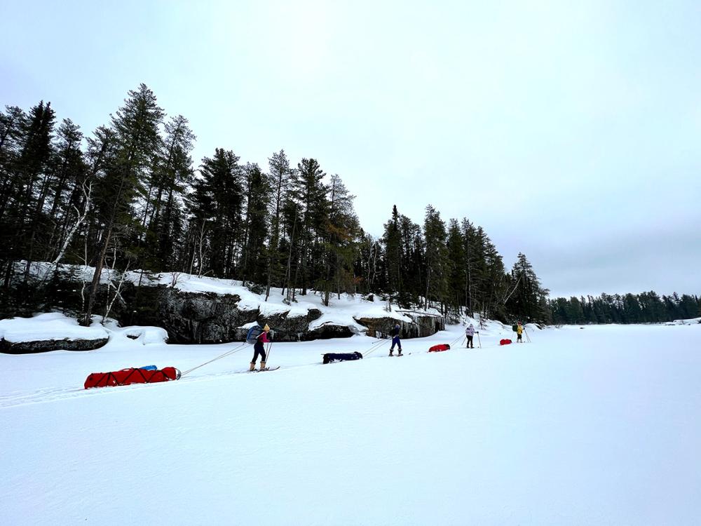 A group pulls toboggans full of winter gear along Lake One.