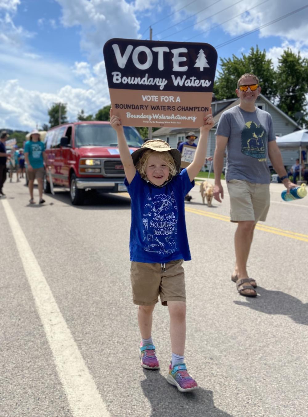 young kid with sign walking parade on sunny day