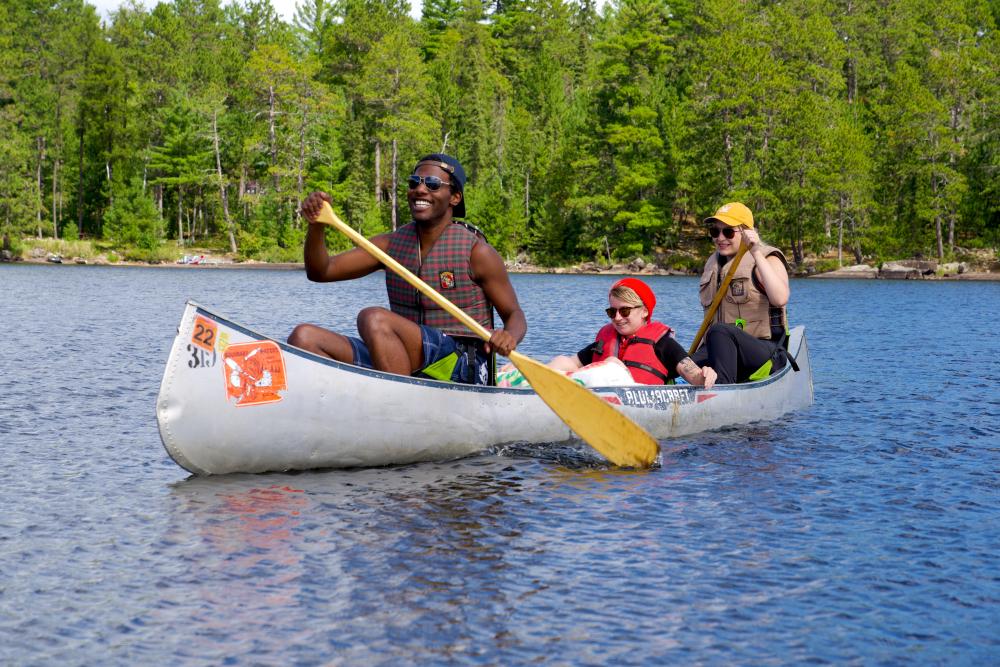 Young people sit in an aluminum canoe in the Boundary Waters during a clear, sunny day