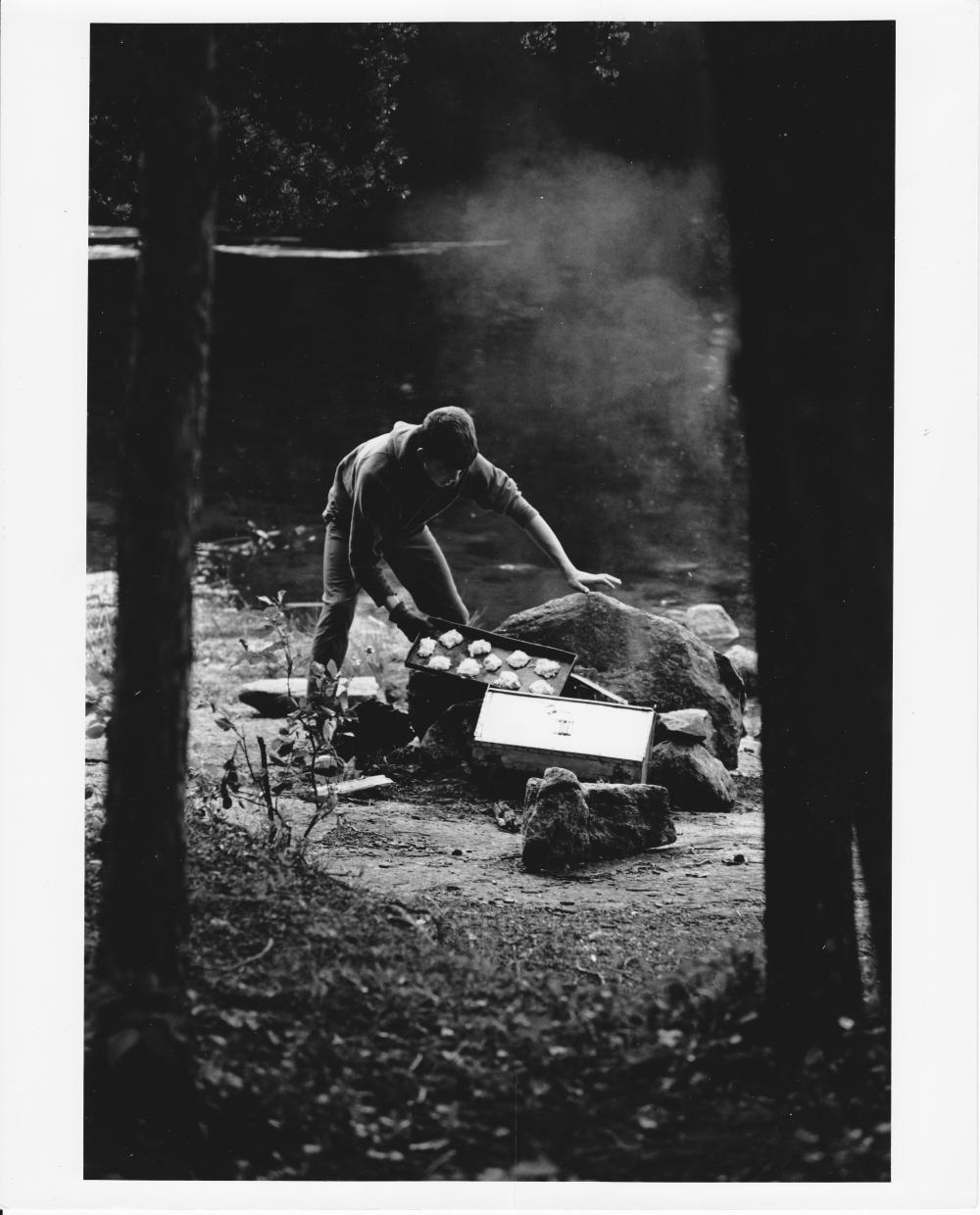 A man prepares to put a tray of biscuit dough over a fire at a campsite in the Boundary Waters