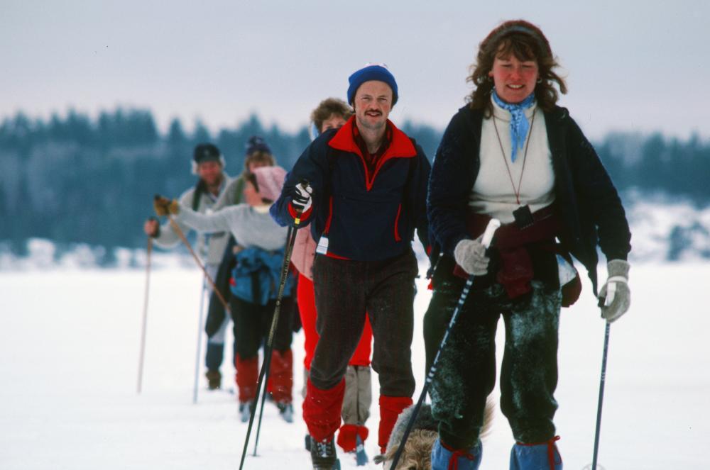 In a single-file line, 6 people cross-country ski on a Boundary Waters lake