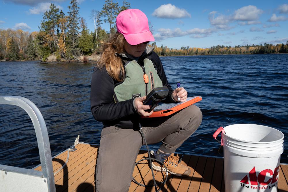 Water quality specialists records data on a clipboard near a lake.