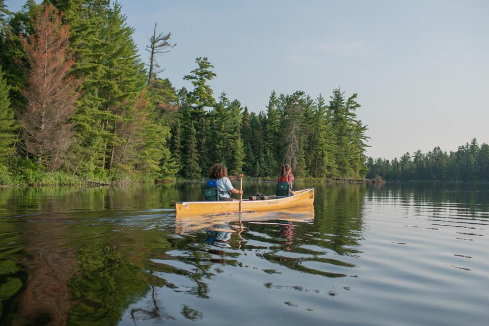 Two people canoe away from shore on a lake