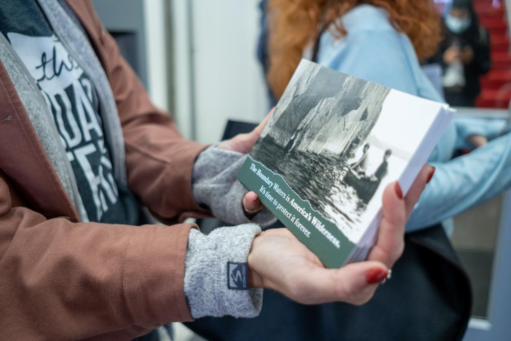 A close-up photo of someone holding a stack of green postcards that read "The Boundary Waters is America's Wilderness"