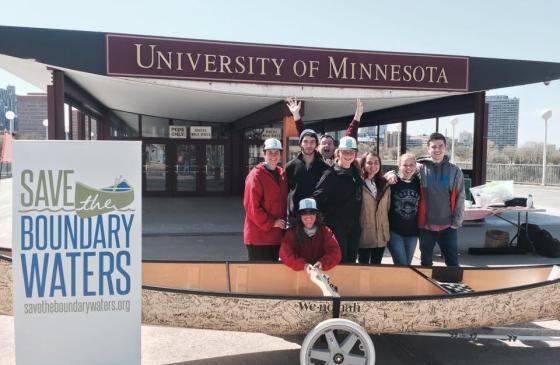 Group of people standing behind a signature canoe at the University of Minnesota