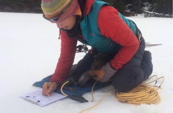 Photo of Amy Freeman kneeling on snow writing on clipboard
