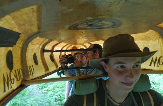 Amy Freeman portaging a canoe with 2 people under the canoe taking a photo of her