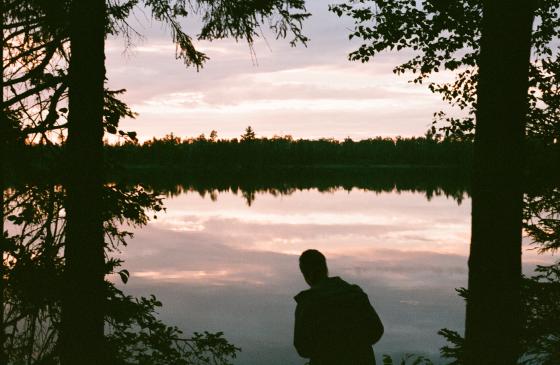 Image of person standing between two tree silhouettes looking out at pink boundary waters sunset