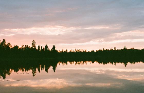 Photo of Boundary Waters sunset with light pink and blue sky and tree silhouettes on horizon