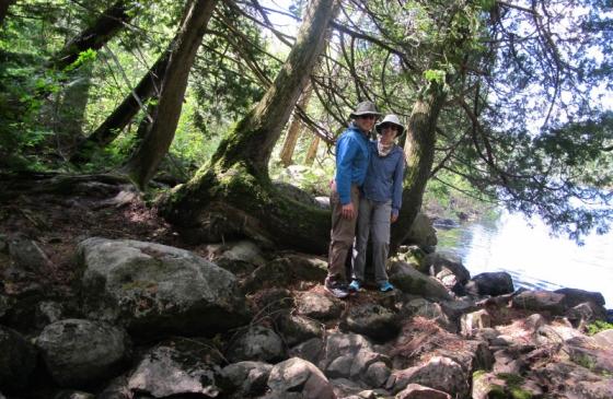 Photo of two people standing under trees on some rocks, smiling