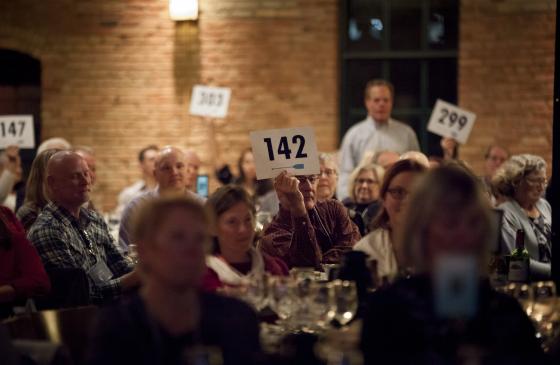 Photo of auction bidder sitting at table holding up sign with "142" on it