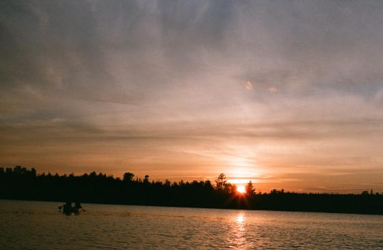 Film picture of soft orange Boundary Waters sunset with silhouette of person paddling canoe