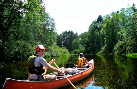two teenagers paddling a red canoe