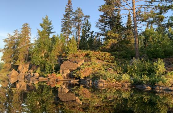 photo of clif-like rocks and trees reflecting onto still water