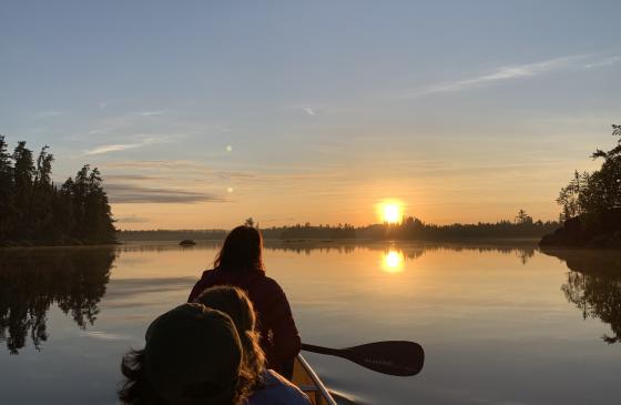 image of backs of three people paddling into the sunrise with sun on the horizon