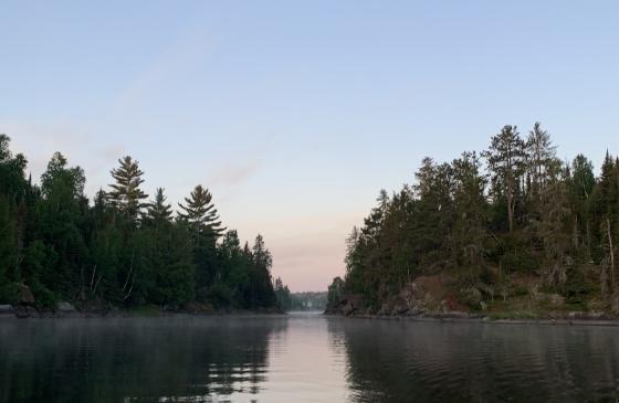 photo of a chanel of water going between 2 islands with trees reflecting on calm water