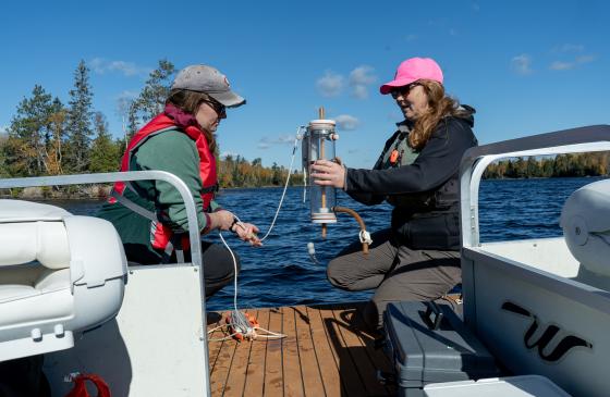 Two researchers handle water quality testing eqipment near a lake. 