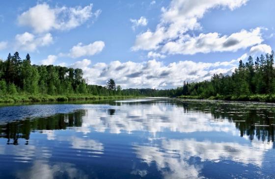 Image of blue sky with white fluffy clouds reflecting onto still water in Boundary Waters