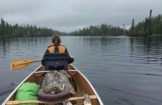 Photo of the back of a youth at the front of a canoe, paddling