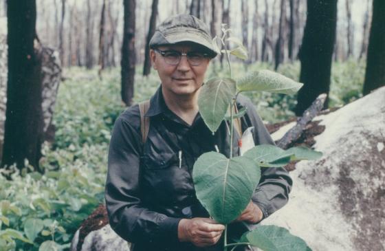 Bud Heinselman wearing glasses and a cap holding a leaf