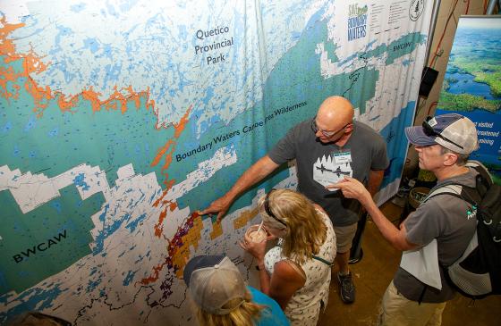 Photo of 3 people around ED Tom Landwehr pointing at BWCA map on wall