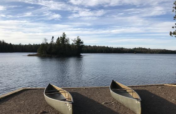 Photo of 2 canoes sitting next to eachother on the shore of a lake