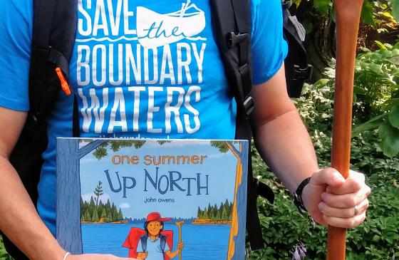 photo of a person holding a canoe paddle and a childrens book reading "one summer up north"