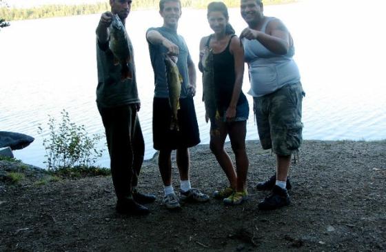 Photo of 4 people holding out fish near waters edge