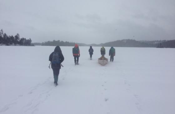 Photo of 5 people walking on snow covered Boundary Waters lake pulling canoe behind them