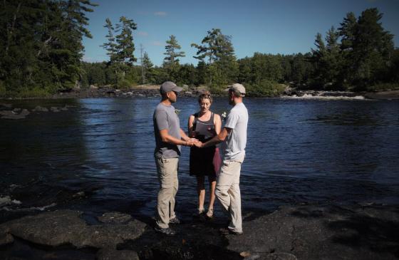Photo of 2 men holding hands getting married infront of a woman in the Boundary Waters