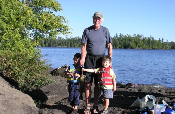 Picture of older man standing between two young kids on shore of the Boundary Waters