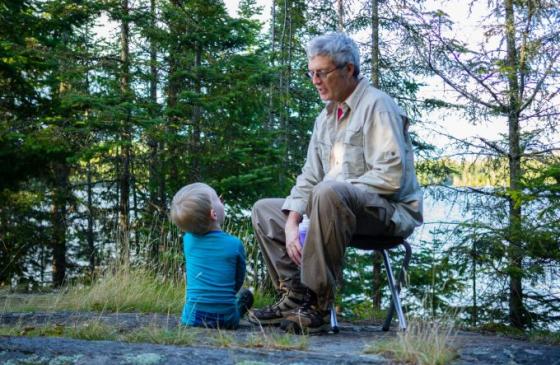 Photo of an older man sitting on a stool and a kid looking up at him smiling