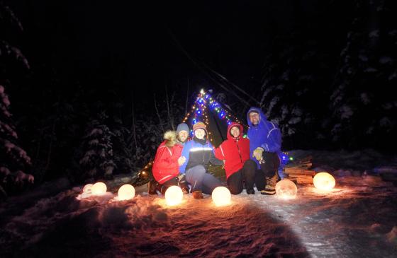 5 people sitting around luminaries infront of a tent with lights strung on it 