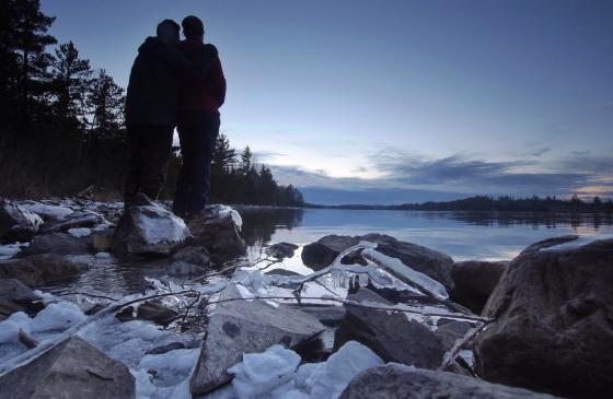 two people stand on rocky waterfront over looking horizon