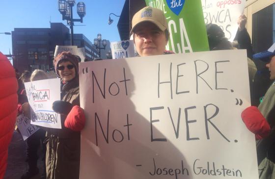 Photo of Amy Freeman holding sign that reads "Not here. Not ever. -Joseph Goldstein"