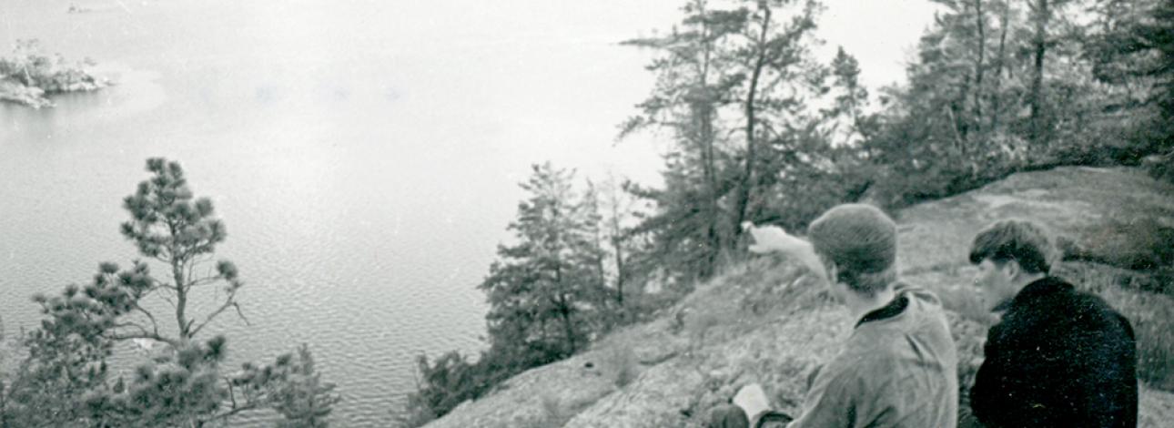 Two men sitting on a rock looking out at a lake. From 1960's
