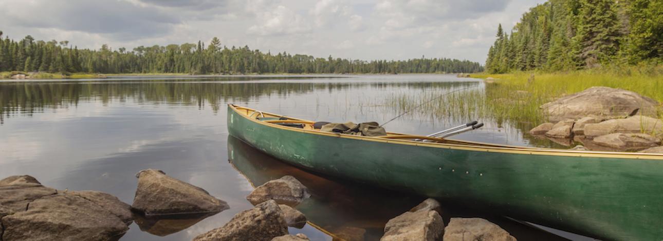 A green canoe sits on the edge of a lake in the Boundary Waters
