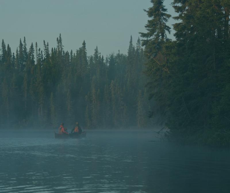 Couple paddling on lake with pines surrounding them with blue overlay 